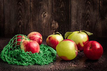 Ripe green and red apples in a green eco-bag on a dark background. Fresh harvest of apples on the table on a dark background.