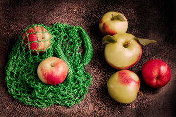 Ripe green and red apples in a green eco-bag on a dark background. Fresh harvest of apples on the table.