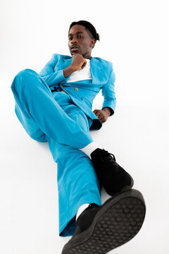 Handsome African Man Laying On Floor Wearing Blue Smart Suit Looking At Camera Sirously On White Background In Studio Isolated Shooting Process For Fashion Magazine.