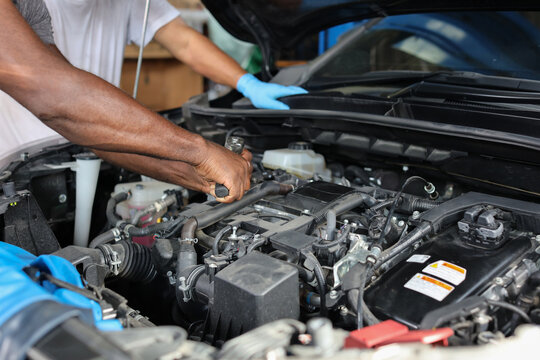 Man technician car mechanic hamds in half uniform checking maintenance a car service at repair garage station. Worker holding wrench and fixing breakdown vehicle. Concept of car center repair service.