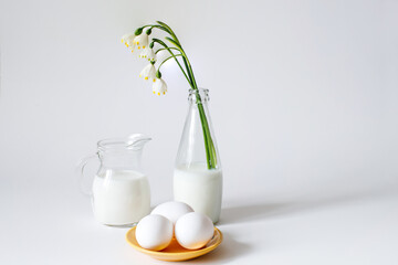 Glass of milk, eggs and flowers on a white background. Still life in soft white color and green...