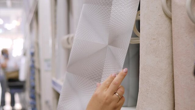 Close-up of a woman choosing and looking at wallpaper for a new renovation in a hardware store.
