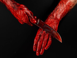 A man wipes a bloody knife with his hand on a black background. 