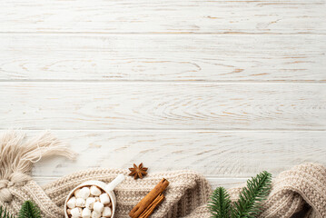 Winter aesthetic concept. Top view photo of pine branches cup of cocoa with marshmallow cozy knitted scarf anise and cinnamon sticks on white wooden table background with empty space