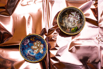 round cups from china with drawings of flowers and patterns black and blue plate on a pink sparkling background top view flat lay