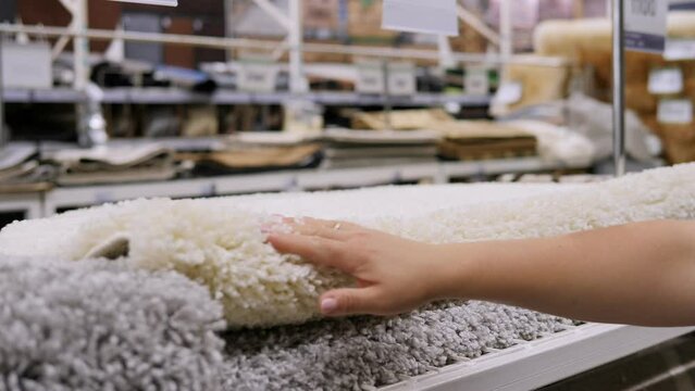 Close-up of a woman touching and choosing carpets in a construction hypermarket or a home store.
