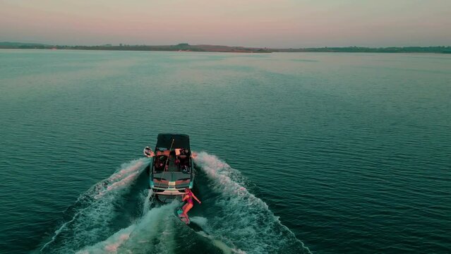 Aerial view of a young sporty girl on wakesurfing at boat with leaving trail on water surface