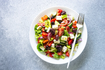 Greek salad with olives, feta cheese and fresh vegetables. Top view on light stone table.
