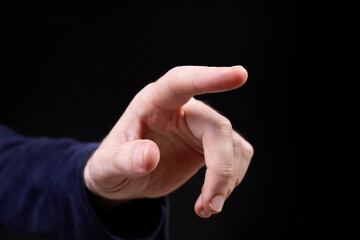 The finger of a male hand points to something on a dark background