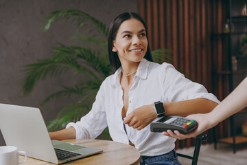 Young happy woman wears white shirt hold pay waiter hold smart watch wireless bank payment terminal...