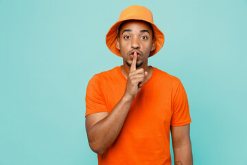 Young secret man of African American ethnicity wear orange t-shirt hat say hush be quiet with...
