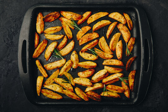 Roasted potatoes. Baked potato wedges in frying tray on dark stone background. Top view with copy space.