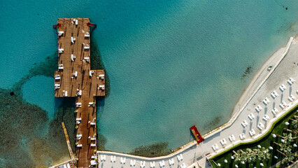 Aerial drone view to the beach with white sand, pier with sunchairs and sea. Luxury summer vacation and resort.