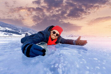 Fototapeta na wymiar Portrait happy male tourist in red hat with shard of transparent ice in winter on Lake Baikal sunset
