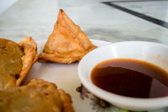 Samosa with tamarind sauce or chutney. A samosa or singara is a fried or baked pastry with a savory filling, including ingredients such as spiced potatoes, onions, and peas. Uttarakhand India.