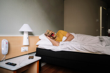 Man with lizard mask in a hotel bed.