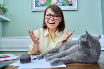 Positive woman looking at webcam, home workplace with pet sleeping cat