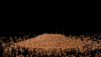 A pile of buckwheat groats is sprinkled on a table on a black background. Selective focus.