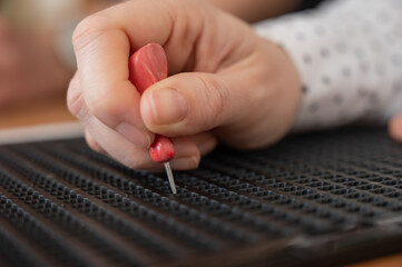 A woman uses a special stencil and stylus to write a letter in braille. 