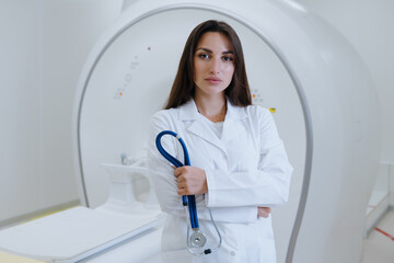 Portrait of a nurse in a white coat holding a stethoscope against the background of a CT scanner in the clinic.