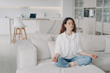 Hispanic woman practicing yoga, meditates, doing breathing exercises on comfortable sofa at home