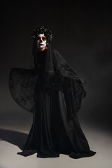 full length of woman in spooky santa muerte costume and catrina makeup on dark background.