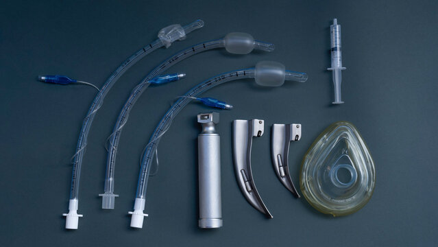 tracheal intubation kit: laryngoscope, several laryngoscope blades and several endotracheal tubes, a syringe to inflate the cuff of the tube. on a dark background, close-up