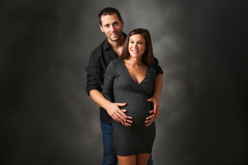 man hugging his pregnant wife from behind they are happily waiting for their baby