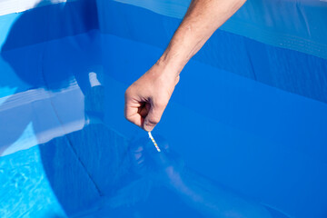 Pool test strips in man's hand. Blue pool background. Water balance.