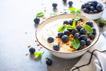 Greek Yogurt with granola and blueberies at light kitchen table.