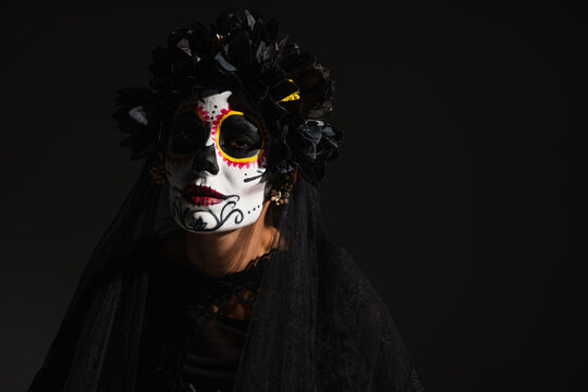woman in halloween costume and sugar skull makeup looking at camera isolated on black.