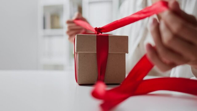 Female hands open unpack gift gift box red ribbon bow on a gift box on a holiday. Gentle scene of opening a gift on a light background. gift for valentine's day new year birthday wedding anniversary
