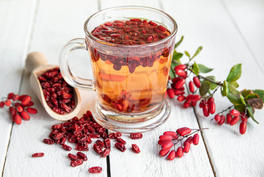Berberis vulgaris also known as common barberry, European barberry or barberry tea drink in class mug in home kitchen. Dried and fresh berries for decoration on vintage white wood board background.
