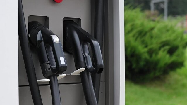 Close-up of young woman's hand puts an electric car charging port at public charging station. Ecology conservation concept, future technologies, electric vehicles, alternative energy Slow motion