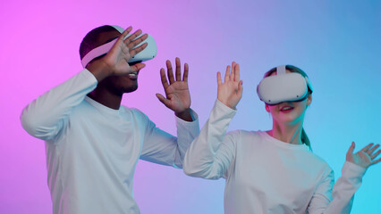 Multiethnic couple in vr goggles and white clothes dance isolated over neon background