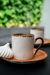 Cup of Turkish black frothy coffee on a black stone table with branches of wild ivy in the background, bizet next to the cup. Vertical frame, selective focus