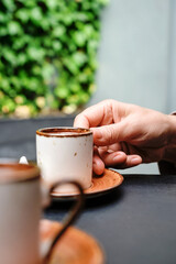 A woman takes a cup of coffee, Turkish black frothy coffee on a black stone table with branches of wild ivy in the background. Vertical frame, selective focus