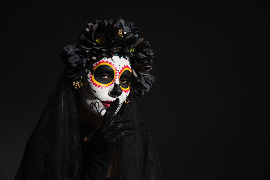 woman in mexican day of dead costume and makeup showing hush sign isolated on black.