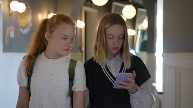 Schoolgirls use smartphone and talk walking in school corridor 