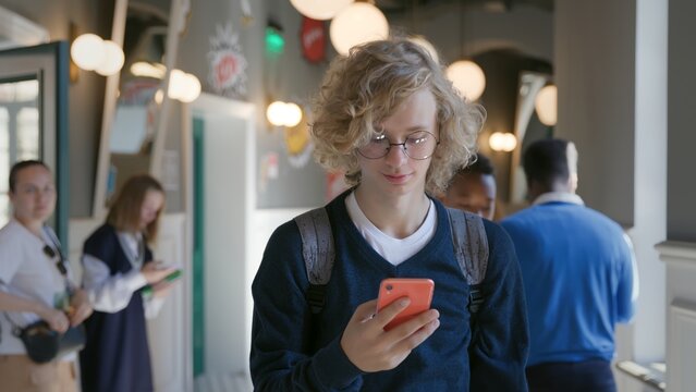 Male high school student looking at smartphone at break walking in corridor