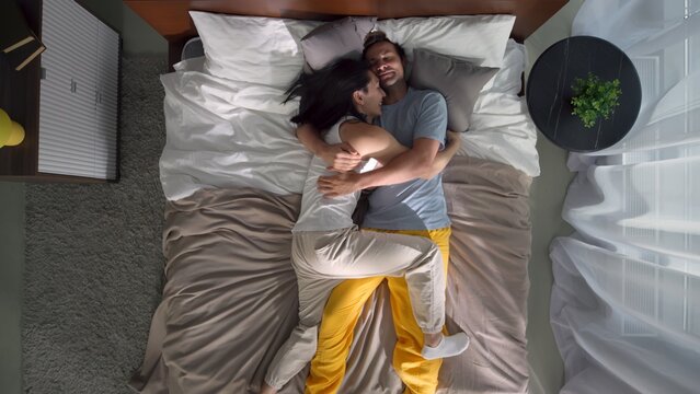 Top view of diverse gay couple lying down in bed and hugging