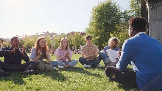 High school students sit on glass and applaud to teacher having outdoor lesson