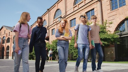 Obraz premium Cheerful multi-racial group of students talking and walking with books outside school. 