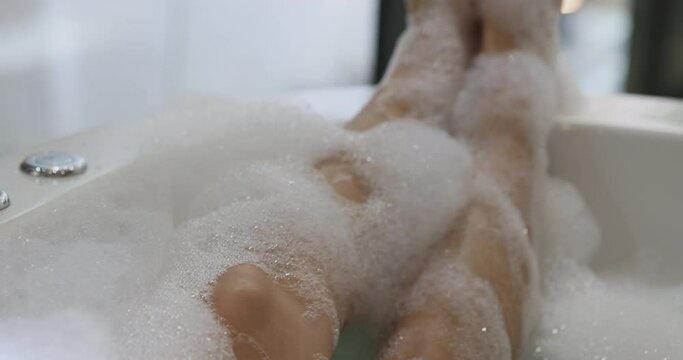 Close up 4K Video relaxing foot in bath tube with bubble foam. Background concept for bathroom and spa relaxing.