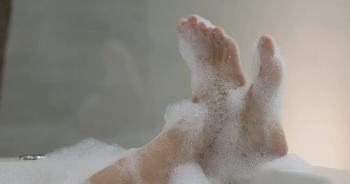 Close up 4K Video relaxing foot in bath tube with bubble foam. Background concept for bathroom and spa relaxing.