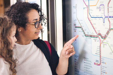 A young mother and daughter looking and pointing at a city metro underground map