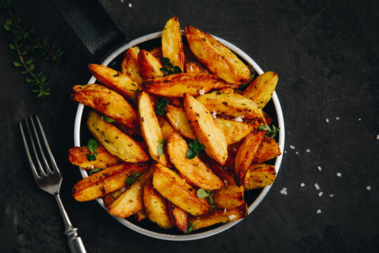 Roasted potatoes. Baked potato wedges in frying pan on dark stone background.