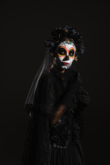 woman in sugar skull makeup and dark halloween costume with veil looking away isolated on black.