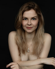 Fototapeta premium Vertical portrait of positive, confident, delightful young naked blonde woman with necklace in black studio. Waist up