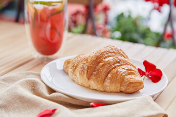 Traditional french fresh croissant on the plate and cold strawberry mojito cocktail at the terrace. Aesthetic morning